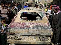 Residents gather around a car damaged in an US air strike in Sadr City, Baghdad, 27 September 2004