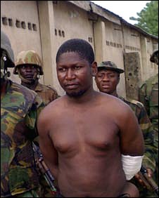 Mohammed Yusuf, bare-chested and with a bandage on his arm, surrounded by soldiers