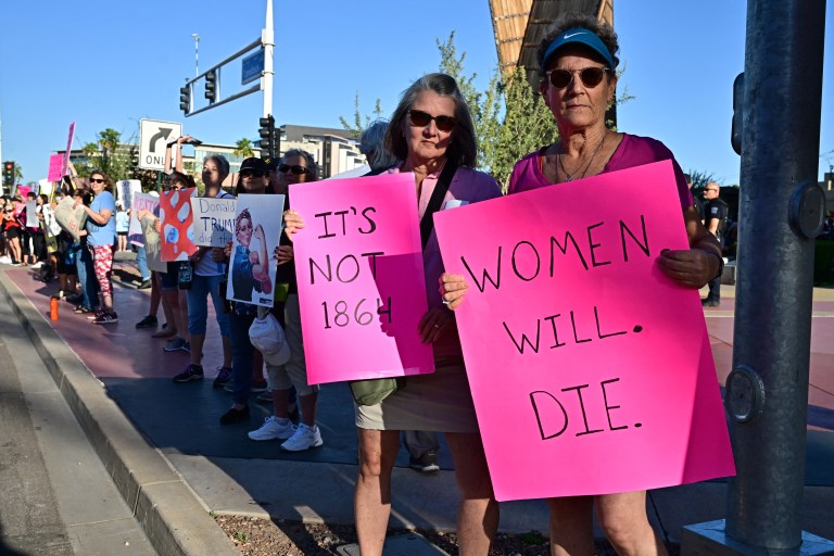 Pro-abortion rights demonstrators rally in Scottsdale, Arizona on April 15, 2024. A woman in the foreground holds a poster with the words "Women. Will. Die." written on it.