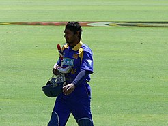 A man wearing blue srilankan jersey holding a bat and a helmet