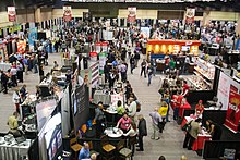 Overhead view of a trade show with dozens of colorful booths with products on display, and people walking between them