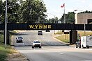 A railroad bridge crosses over a four-lane highway, with the bridge painted "Welcome to Wynne, The City with a Smile"