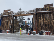 A tall wooden gate covered in snow, with a traffic controller in midground and crane with crew members in background