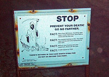 A white warning sign with a picture of the Grim Reaper and the headline "Prevent your death. Go no farther" over black text explaining the dangers to divers of proceeding into the cave without proper equipment and certification.