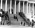 Pall bearers carrying the casket of President Kennedy up the center steps of the United States Capitol Building, followed by a color guard holding the flag of the president of the United States, and the late President's widow, Jacqueline Kennedy and her children, Caroline Kennedy and John F. Kennedy Jr., on November 24, 1963.