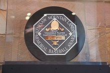 A black circle with an octagonal read "KENESAW MOUNTAIN LANDIS MEMORIAL BASEBALL AWARD". In the middle of the octagon is a baseball diamond which contains, from the top, Judge Landis' face in gold, "Most Valuable Player", the winner's league, his name in a gold rectangle, and his team.