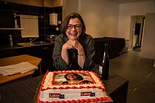 Kearney smiling while standing over a cake. The cake is decorated in Labor party colours, and features a picture of Kearney.