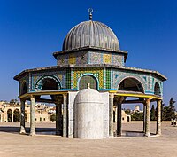 A gray metal-domed octagonal structure decorated with tiles of different colors and geometric designs, supported by dark stone columns with beige-colored capitals