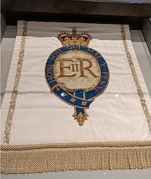 light-colored cloth banner with the initials E R II surrounded by the words 'Honi soit qui mal y pense' in a border, beneath a crown