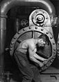 Image 16Lewis Hine's 1920 image "Power house mechanic working on steam pump," which shows a working class young American man with wrench in hand, hunched over, surrounded by the machinery that defines his work.