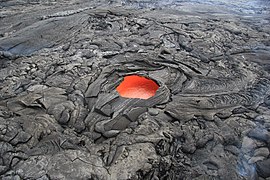 A "skylight" hole, about 6 m (20 ft) across, in a solidified lava crust reveals molten lava below (flowing towards the top right) in an eruption of Kīlauea in Hawaii