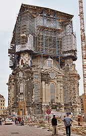 Barevná fotografie zachycující znovupostavení kostela Frauenkirche, na němž je upevněno lešení v podobě krychlového nástavce