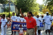Jawando walking and waving in a parade in front of a banner that says "Will Jawando, Democrat for Congress"
