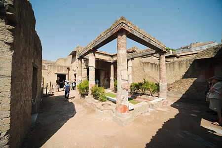 House of the Corinthian Atrium, in Herculaneum. The six pillars are stuccoed tufa, repaired with brick. This atrium is halfway to being a peristyle; planters flank a grassy area. The central marble fountain was fed by an aqueduct, making the original purpose of the atrium, a structure for gathering rainwater, superfluous. The original well remains, beside the nearest pillar (floorplan).