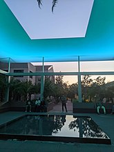 Granite benches and fountain inside the skyspace canopy illuminated blue with an aperture in the center