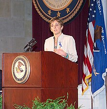 Une femme parle dans deux micros posés sur un pupitre du Departement of Justice américain.