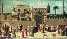 Bustling city scene of men dressed in turbans outside the walls of an Oriental city. An official appears to be holding court at the gate, reclining on a red sofa with two individuals facing him (perhaps parties to a dispute). Others observe the proceedings—many men on foot, two men on camel-back, and one on horse-back. A monkey, a male deer and a female deer are also present in the crowd.