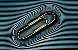 A metal paperclip floating on water. A grille in front of the light has created the 'contour lines' which show the deformation in the water surface caused by the metal paper clip.