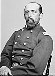 Black and white photo shows a balding, bearded man wearing a dark uniform with two rows of buttons.