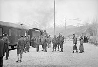 American and British Army train crewmen standing at a station. An American locomotive is seen at the head of the train at left. c. 1943