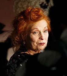 Vivienne Westwood, wearing a sparkly black dress, looking over her shoulder at the camera.