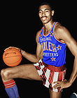 Man in a Harlem Globetrotters uniform is on one knee and holding a basketball.