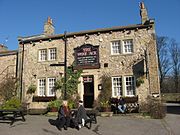 A public house with a sign that says "The Woolpack", with three people sat on benches outside