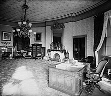 black and white image of the highly ornate yellow oval room with the Resolute desk on the right side of the image.