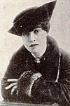 A photograph of Anita Loos, wearing a fur-lined dress and a large dress hat