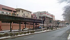 겨울에 도시 거리 위에 두 개의 건물이 있는 고가 철도 선로. 왼쪽에 있는 작은 것은 옅은 노랑색이고 좁다. 오른쪽에 있는 큰 것은 회색이고, 빨간색 줄무늬가 있으며, 상자 모양이며 선로 위로 솟아 있다.