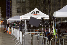 Press tents and cameras behind crowd control barriers, on a sidewalk
