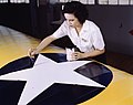 Una donna dipinge la coccarda dell'aviazione su un'ala di un aereo durante la seconda guerra mondiale