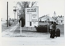 Two women walk past a large sign in Vietnamese and English at an army base