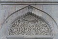 An intricately carved marble tympanum above an exterior window of the mosque