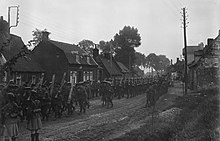 A long column of soldiers march through a village