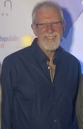 Man with glasses and a blue shirt is staring at the camera.