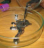 Un líquido prateado parecido á melaza que se verte nun recipiente circular cunha altura equivalente a unha moeda máis pequena no seu bordo