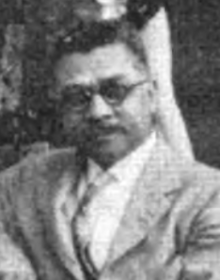 An African-American man, wearing glasses, a mustache and a light-colored suit