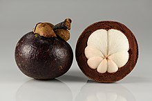 Photograph of a whole mangosteen fruits, and one partially peeled to show the horizontal cross section which reveals the white internal flesh divided into seven sections.