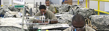 Prisoners sit at sewing machines, sewing military uniforms