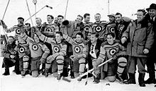 Black and white photo of a team hockey players holding their sticks in the air and dressed in jerseys adorned with the Royal Canadian Air Force logo