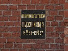 A black plaque with gold letters on a brick wall with a Russian inscription that translates as Grigory Konstantinovich Ordzhonikidze, 1886-10-28–1937-02-18