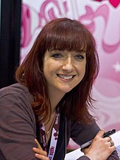 Photo of a smiling woman with medium length red hair and a purple shirt.