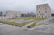 Barevná fotografie s pohledem na dvě moderní geometrické budovy z betonu