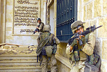 Fotografia colorida de três fuzileiros navais dos EUA entrando em um palácio parcialmente destruído
