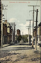 A street with buildings and hydro lines on both sides. There is a horse and buggy parked on the street.
