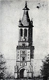 Drawing of a tall tower with a clock and a tapering pyramidal roof; a status is located on top of the pointed roof