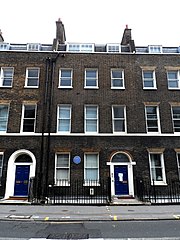 An unassuming brown brick row house marked with a blue plaque