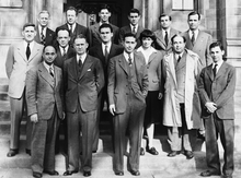 14 men and one woman, all wearing formal suit jackets, with Szilard also wearing a lab coat