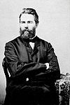 A photograph of Herman Melville seated at a chair, arms crossed and sporting combed-back hair and a blocky beard